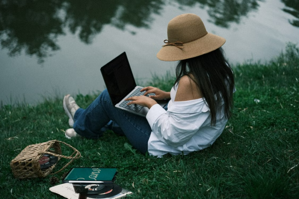 Freelancer working on a laptop on the grass beside a lake
