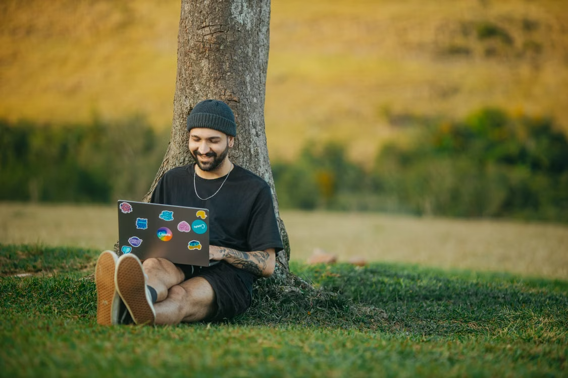 Smiling freelancer working on a laptop while sitting under a tree