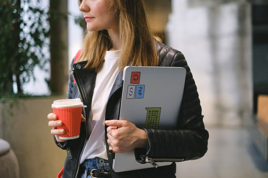 Freelancer holding a laptop covered in coding stickers and a coffee cup